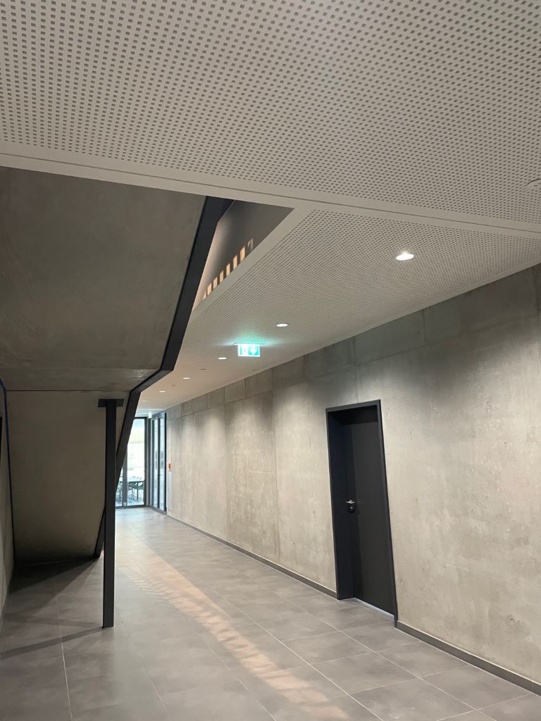 Gelochte Akustikdecke an einer Sichtbetonwand